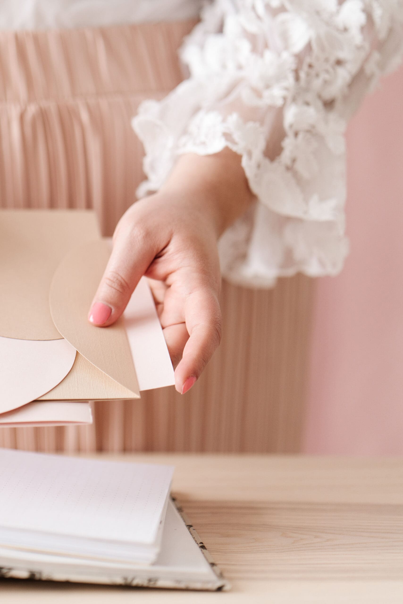 Close-up of woman placing a pastel envelope onto a stack of deckled-edge paper on a wooden desk -Laura Keenan-Nervous System Coach